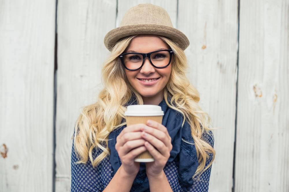 Frau mit Hut und Brille, die einen Kaffeebecher hält